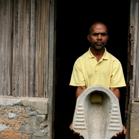 Antonia Dos Santos holds up a toilet in front of his home