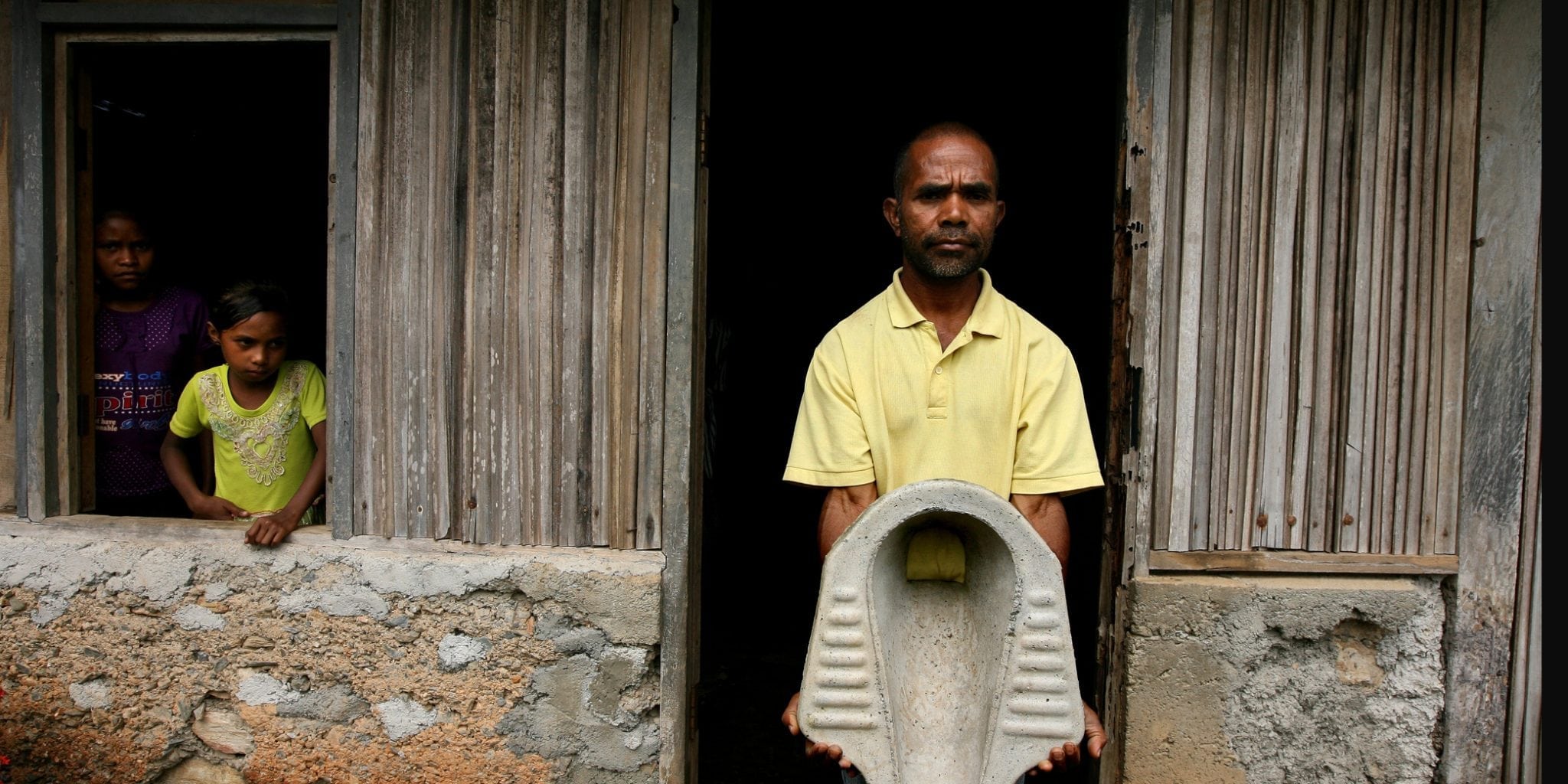 Antonia Dos Santos holds up a toilet in front of his home