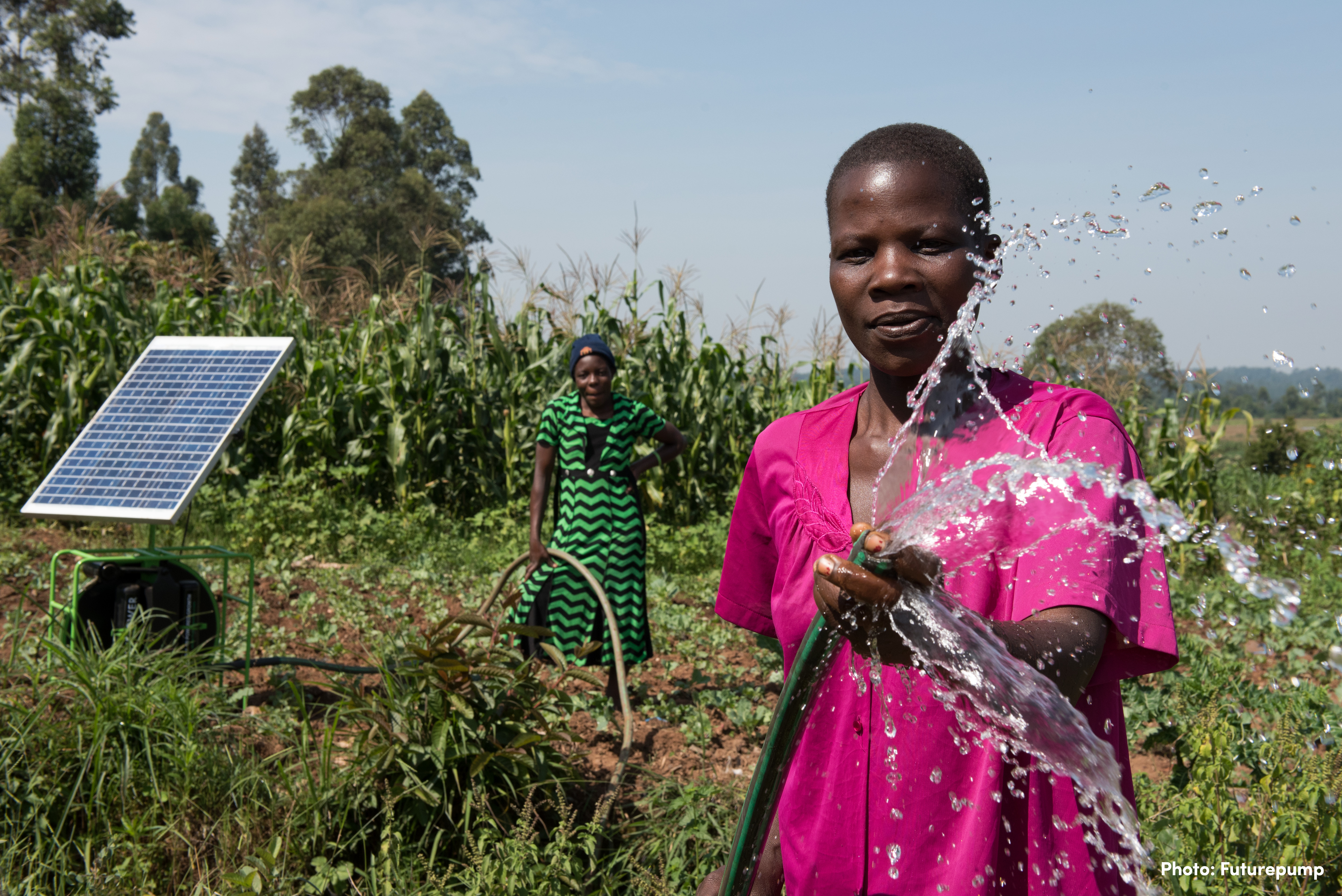 Two women use a solar-powered irrigation pump in a field.