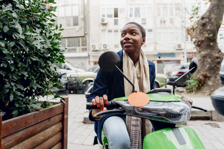 Portrait of a young and stylish african woman with a moped in the city