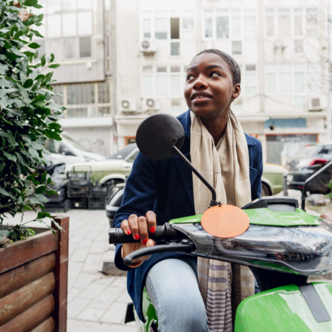 Portrait of a young and stylish african woman with a moped in the city