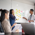 Three people collaborating using sticky notes, a notepad, and a computer.